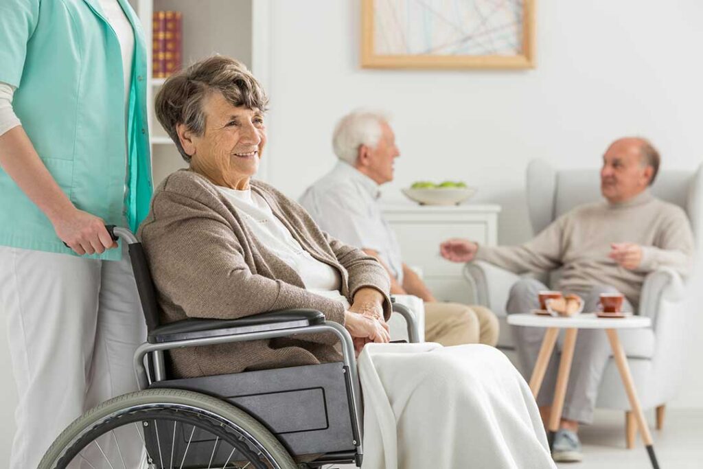 Residents gather around a table, enjoying conversation and board games in a bright, shared living room.